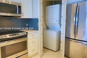 kitchen featuring white cabinets, backsplash, stacked washer / dryer, and stainless steel appliances