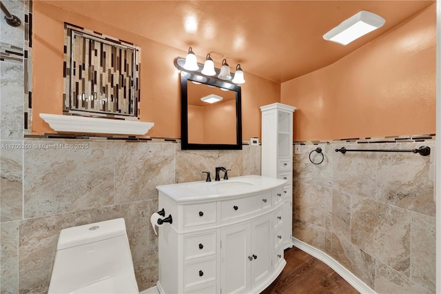 bathroom featuring toilet, a wainscoted wall, wood finished floors, vanity, and tile walls