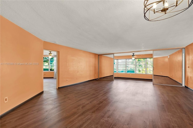 unfurnished living room featuring a textured ceiling, dark wood-type flooring, baseboards, and an inviting chandelier