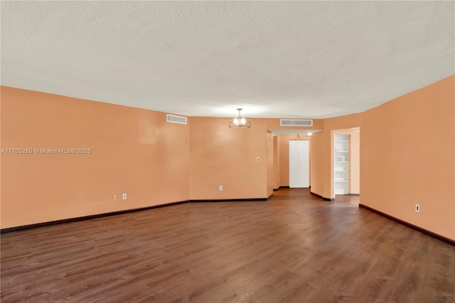 empty room featuring a textured ceiling, visible vents, and dark wood-style flooring