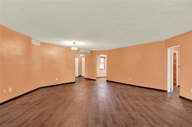 empty room with visible vents, a textured ceiling, baseboards, and wood finished floors