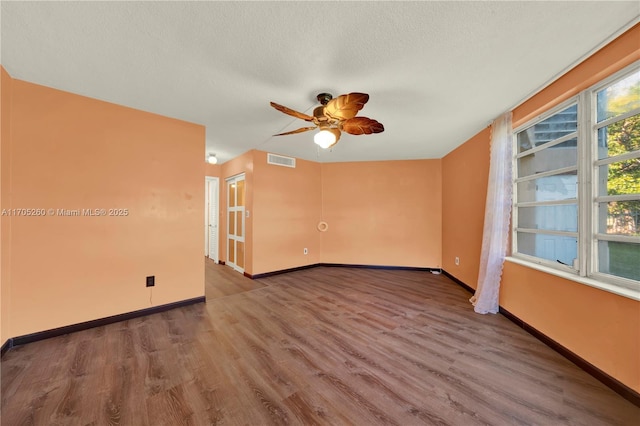 empty room featuring baseboards, visible vents, a textured ceiling, and wood finished floors