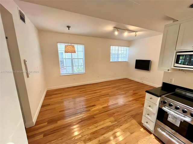 kitchen featuring light hardwood / wood-style floors, built in microwave, pendant lighting, stainless steel stove, and white cabinetry