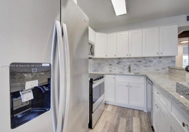 kitchen with appliances with stainless steel finishes, tasteful backsplash, light hardwood / wood-style floors, light stone counters, and white cabinetry