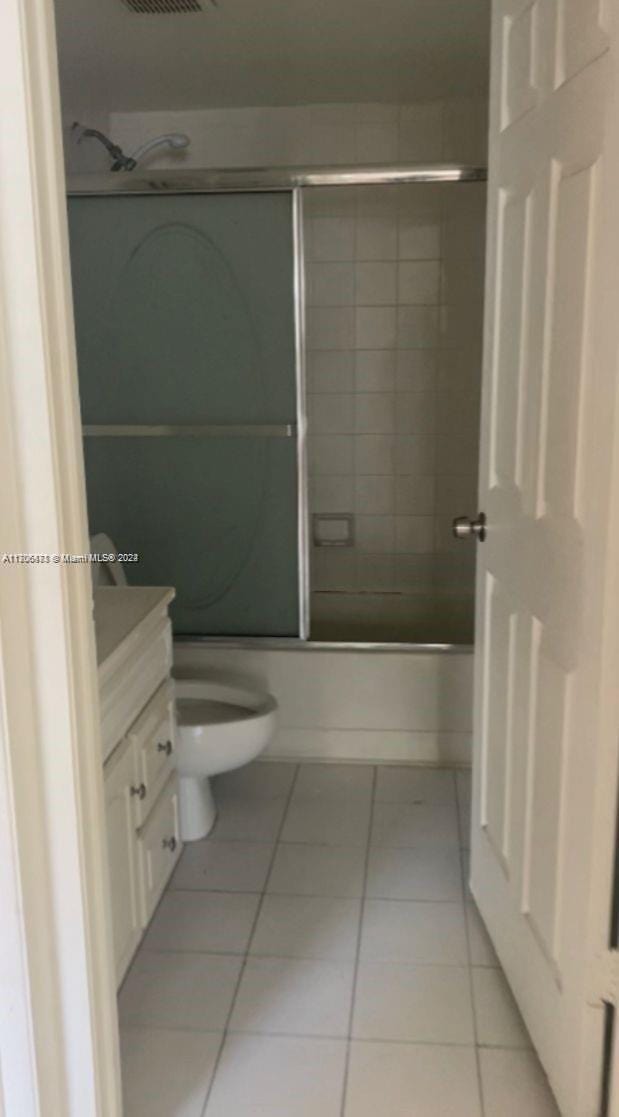 full bathroom featuring shower / bath combination with glass door, tile patterned flooring, vanity, and toilet