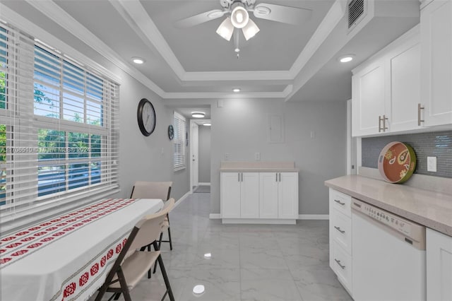 kitchen featuring white dishwasher, a raised ceiling, white cabinetry, and ornamental molding