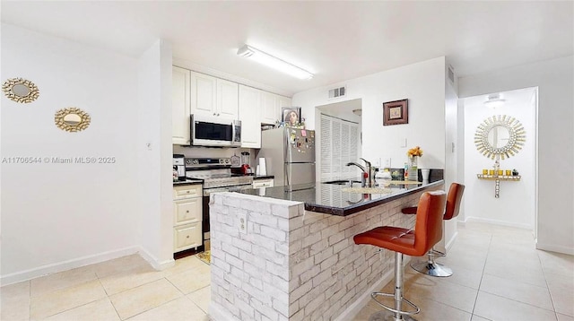 kitchen featuring a peninsula, visible vents, appliances with stainless steel finishes, dark countertops, and a kitchen bar