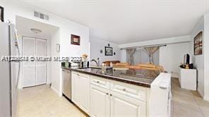 kitchen with stainless steel dishwasher, dark countertops, a sink, and visible vents