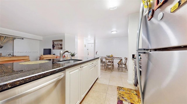 kitchen with stainless steel appliances, white cabinets, a sink, light tile patterned flooring, and dark stone counters