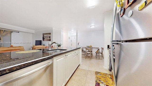 kitchen with light tile patterned floors, stainless steel appliances, a sink, white cabinetry, and dark stone counters