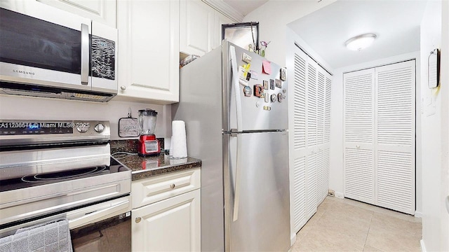 kitchen featuring dark stone countertops, stainless steel appliances, light tile patterned flooring, and white cabinets