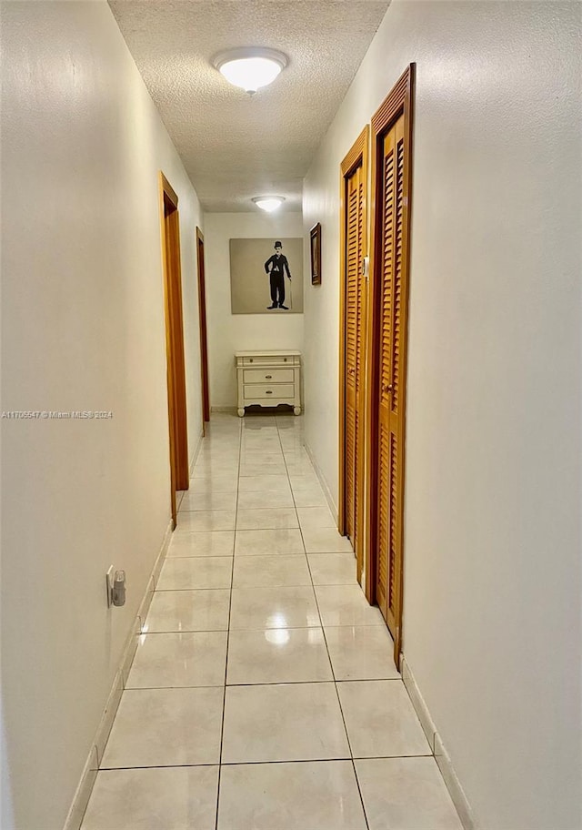 corridor with a textured ceiling and light tile patterned flooring