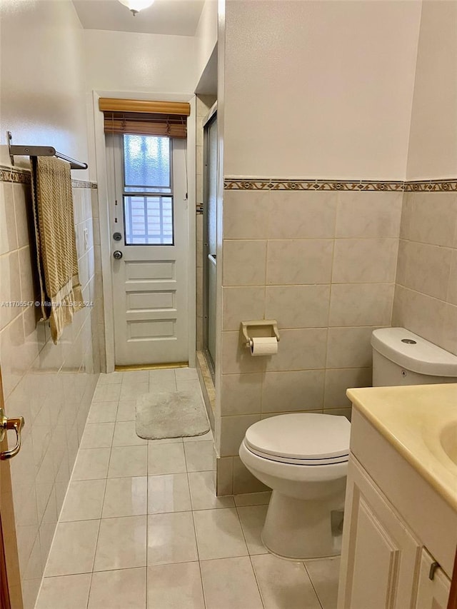 bathroom with tile patterned floors, vanity, a shower with door, tile walls, and toilet