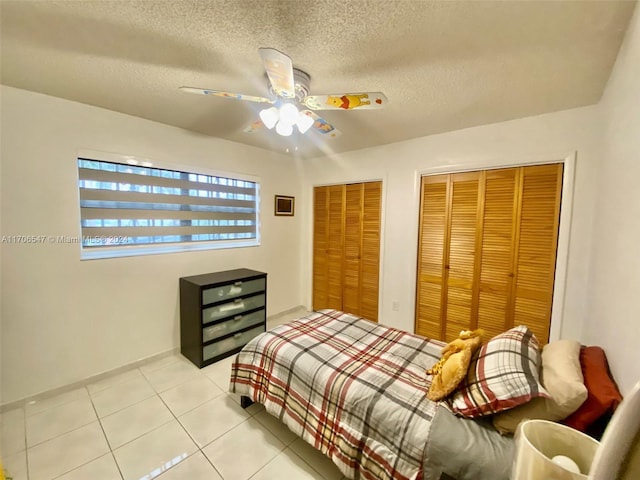 tiled bedroom with a textured ceiling, ceiling fan, and two closets