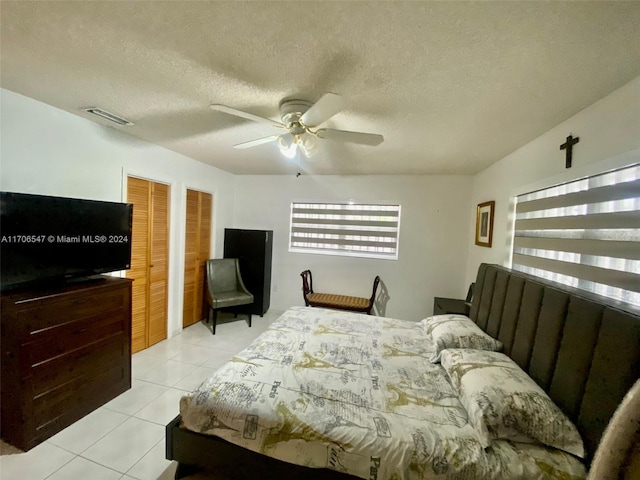 tiled bedroom with two closets, ceiling fan, and a textured ceiling