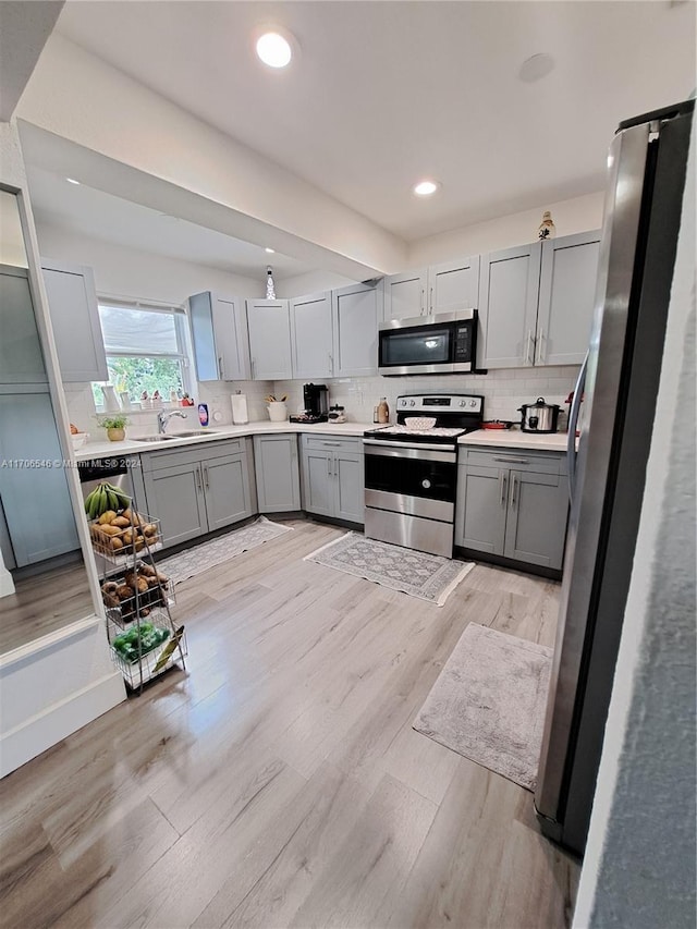 kitchen with sink, stainless steel appliances, backsplash, light hardwood / wood-style floors, and gray cabinets