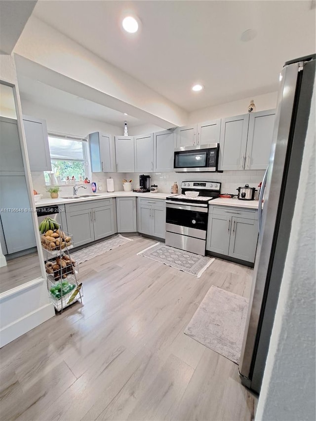 kitchen featuring backsplash, gray cabinetry, stainless steel appliances, sink, and light hardwood / wood-style floors