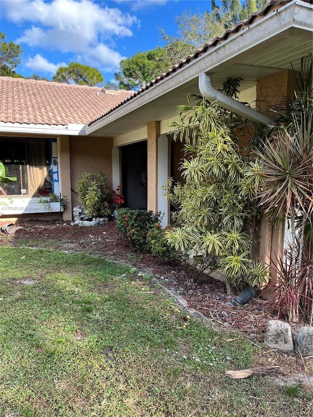 view of exterior entry with a tile roof, a yard, and stucco siding