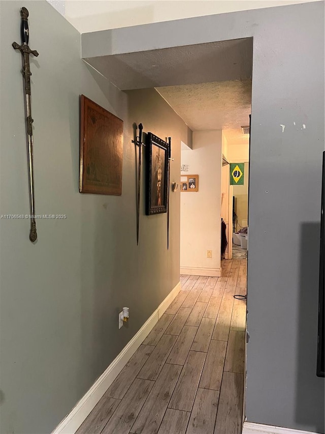 corridor featuring a barn door, wood finished floors, a textured ceiling, baseboards, and visible vents