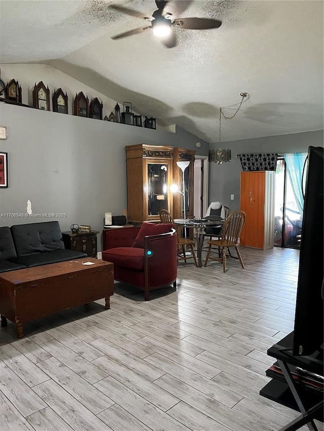 living room featuring light wood-style floors, vaulted ceiling, a textured ceiling, and ceiling fan