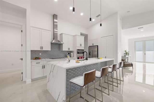 kitchen with wall chimney exhaust hood, white cabinets, an island with sink, and appliances with stainless steel finishes