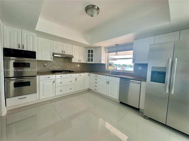 kitchen with white cabinets, appliances with stainless steel finishes, a raised ceiling, and dark stone counters