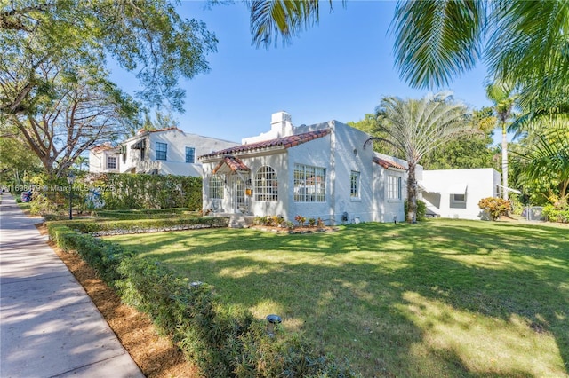 mediterranean / spanish house featuring a tiled roof, a chimney, a front lawn, and stucco siding