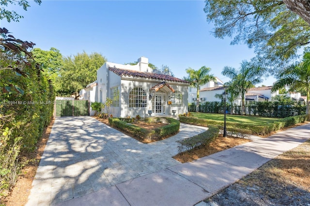 mediterranean / spanish-style house featuring a tile roof, a chimney, french doors, a front yard, and stucco siding