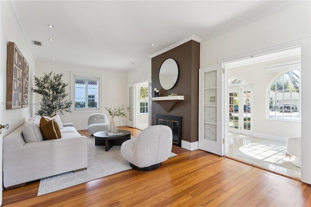 living area with ornamental molding, a fireplace, wood finished floors, and visible vents