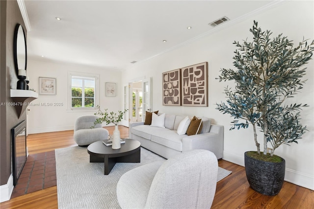 living area featuring a glass covered fireplace, wood finished floors, visible vents, and crown molding