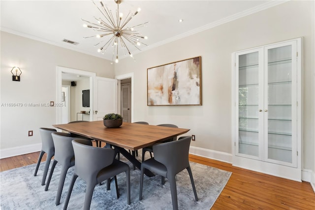 dining area with ornamental molding, wood finished floors, visible vents, and a notable chandelier