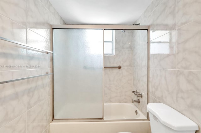 bathroom with shower / bath combination with glass door, toilet, and tile walls