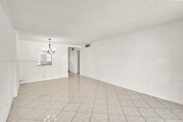 tiled empty room with a textured ceiling and an inviting chandelier