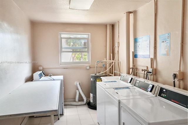 clothes washing area featuring electric water heater, washer and clothes dryer, light tile patterned floors, and a textured ceiling