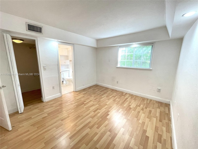 interior space featuring a spacious closet, a closet, ensuite bathroom, and light wood-type flooring