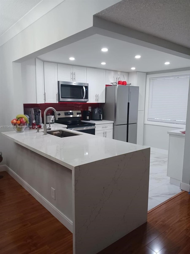 kitchen with light stone countertops, kitchen peninsula, hardwood / wood-style floors, white cabinets, and appliances with stainless steel finishes