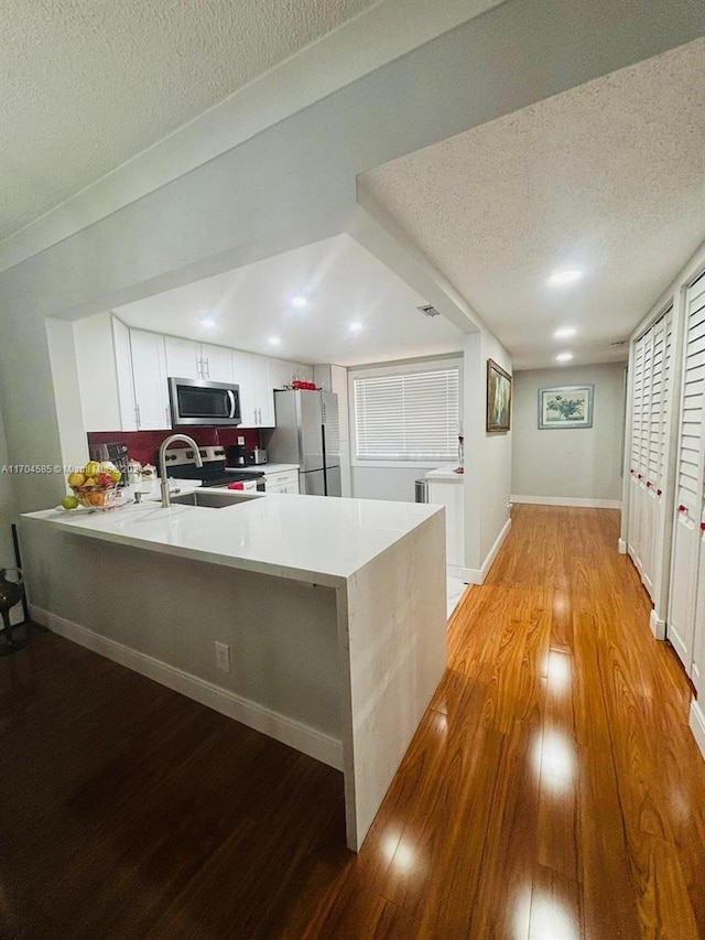 kitchen with kitchen peninsula, appliances with stainless steel finishes, a textured ceiling, and white cabinetry