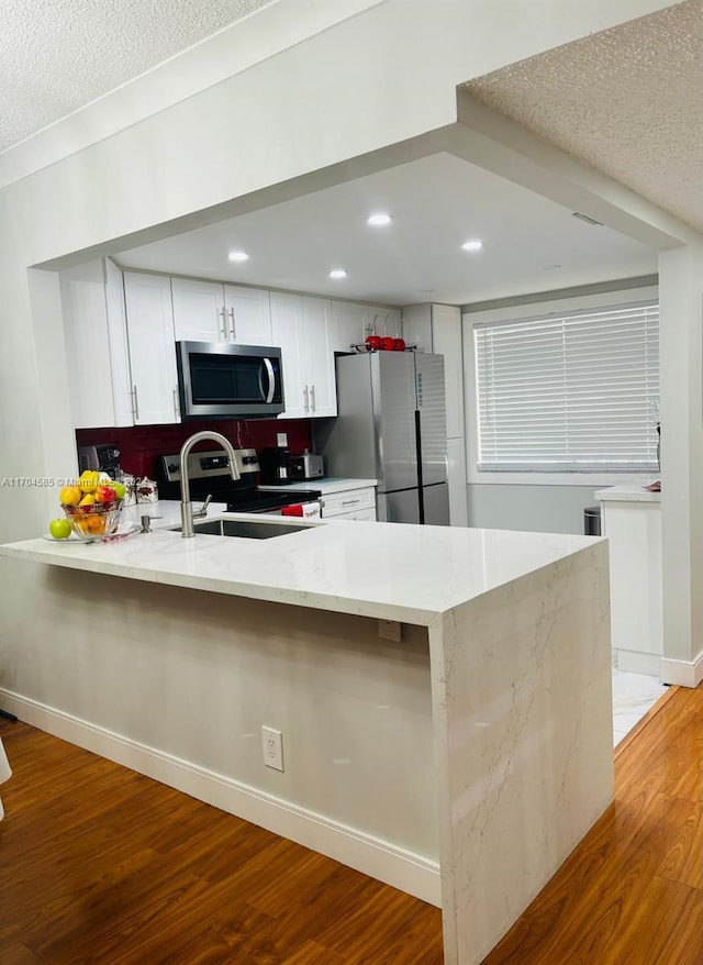 kitchen featuring stainless steel appliances, kitchen peninsula, light hardwood / wood-style floors, a textured ceiling, and white cabinets