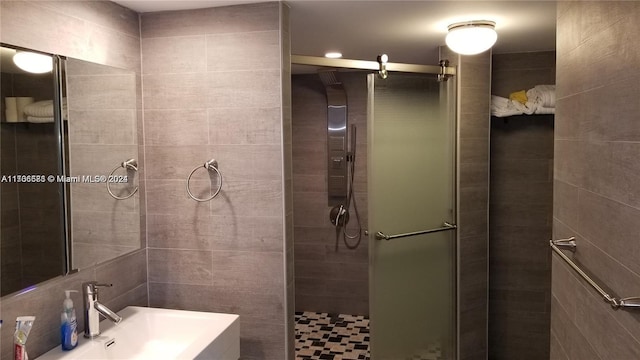 bathroom with sink, a shower with shower door, and tile walls