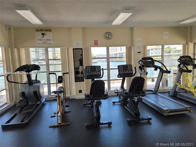 exercise room featuring a textured ceiling and a water view