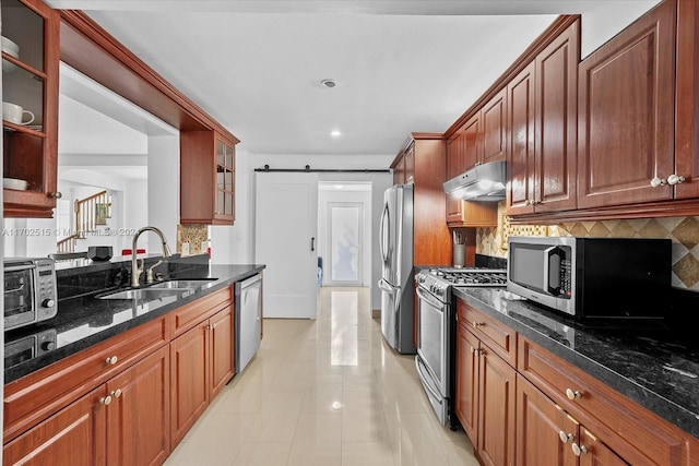 kitchen with dark stone counters, a barn door, sink, and stainless steel appliances