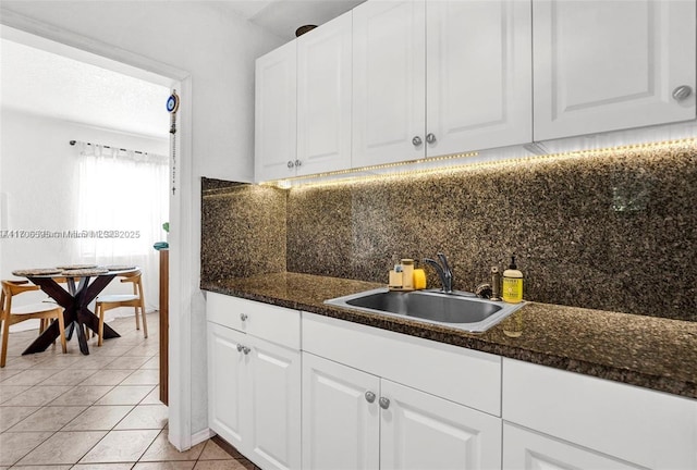 kitchen featuring backsplash, dark stone countertops, sink, white cabinetry, and light tile patterned floors