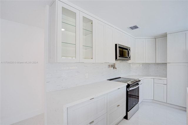 kitchen with white cabinets, decorative backsplash, light tile patterned flooring, and stainless steel appliances