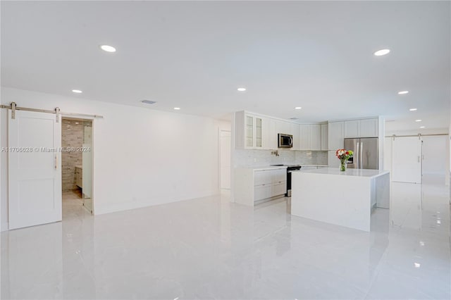 kitchen with backsplash, stainless steel appliances, a barn door, white cabinetry, and a kitchen island