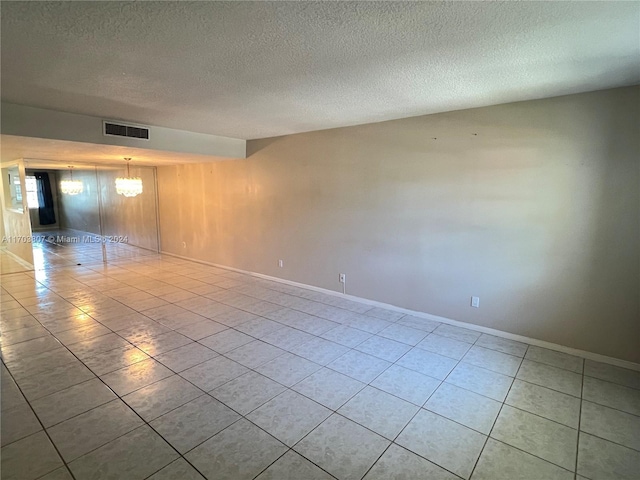 tiled empty room featuring a notable chandelier and a textured ceiling