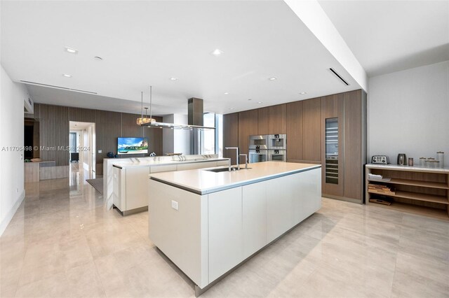 kitchen featuring white cabinetry, sink, an island with sink, pendant lighting, and wooden walls