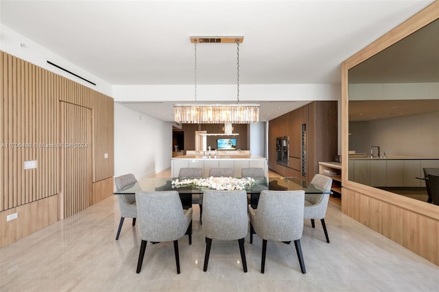 dining space featuring wood walls, sink, and an inviting chandelier