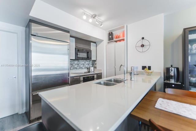 kitchen featuring black appliances, a breakfast bar, kitchen peninsula, decorative backsplash, and sink