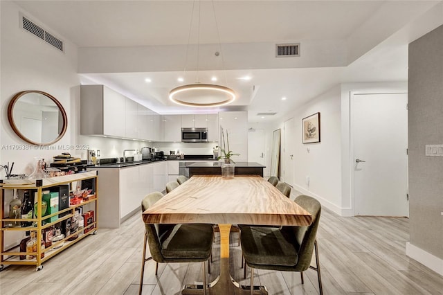 dining space featuring a raised ceiling, visible vents, and light wood-type flooring