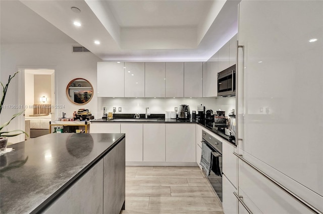 kitchen featuring a raised ceiling, sink, black oven, light hardwood / wood-style floors, and white cabinetry